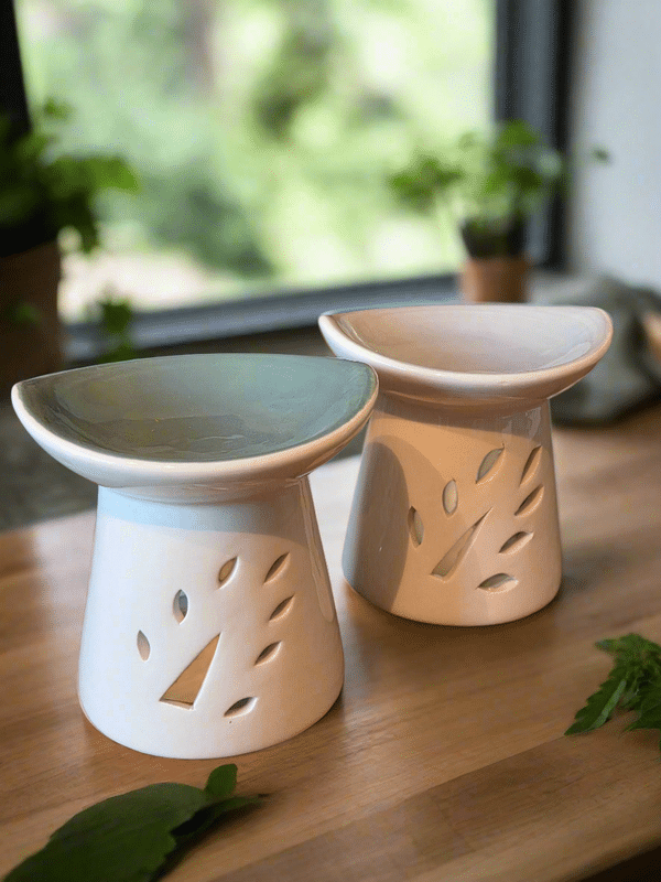 Deux diffuseurs d'huiles essentielles en céramique blanche avec découpes de feuilles sur une table en bois.
